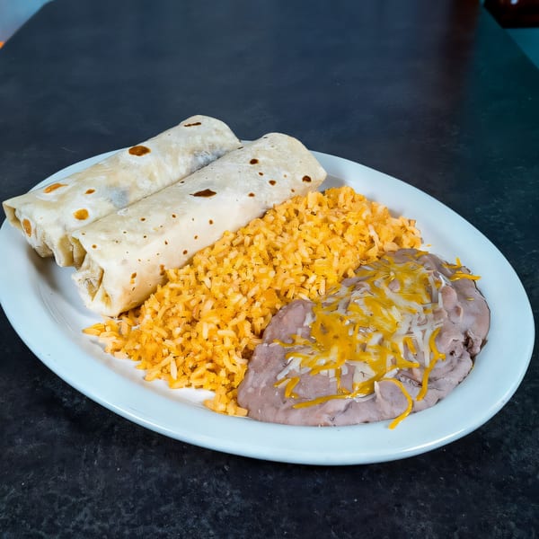 Two burritos with Mexican rice and refried beans topped with melted cheese on a white plate.