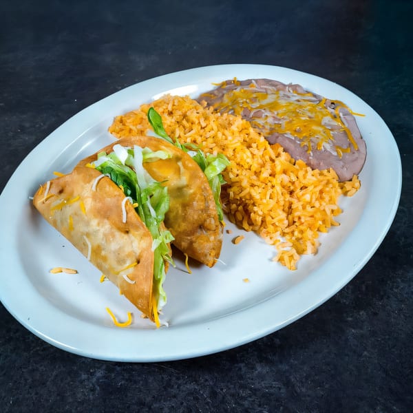 Two crispy tacos with lettuce and cheese, served with Mexican rice and refried beans.
